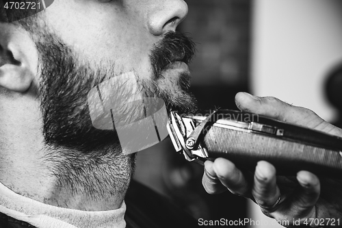 Image of Young handsome barber making haircut for attractive man in barbershop