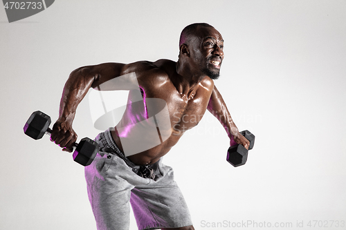 Image of Young african-american bodybuilder training over grey background
