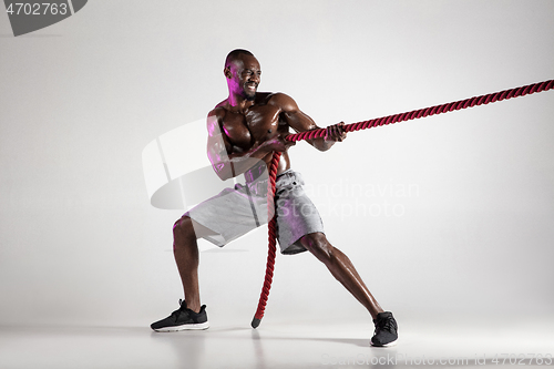 Image of Young african-american bodybuilder training over grey background