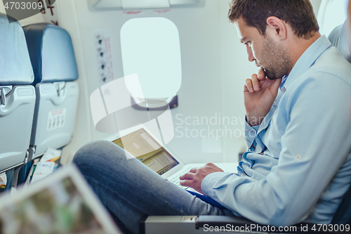 Image of Businessman working with laptop on commercial airplane.