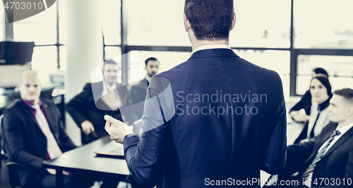 Image of Successful team leader and business owner leading informal in-house business meeting. Businessman working on laptop in foreground. Business and entrepreneurship concept