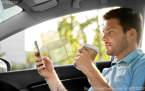 Image of passenger drinking coffee using smartphone in car