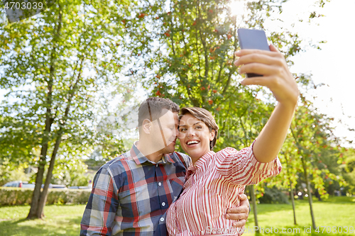 Image of happy couple in park taking selfie by smartphone