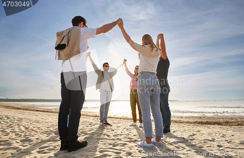 Image of happy friends holding hands on summer beach