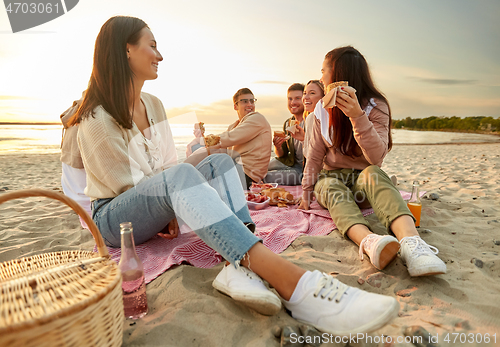 Image of happy friends eating sandwiches at picnic on beach