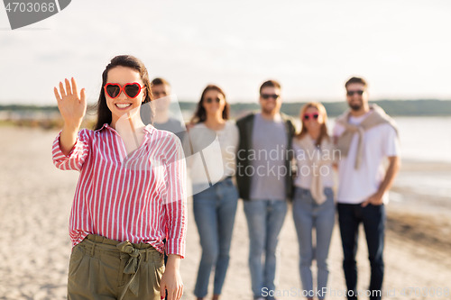 Image of woman with friends on beach in summer waving hand