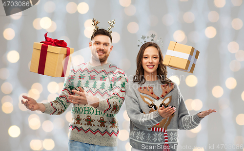 Image of happy couple in christmas sweaters with gift boxes