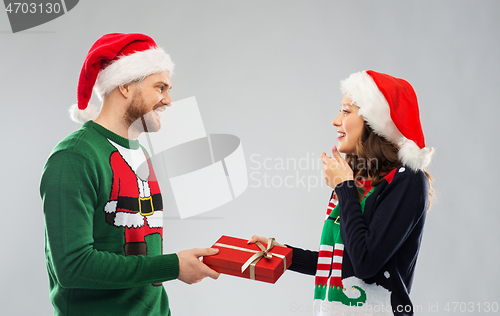 Image of happy couple in christmas sweaters with gift box