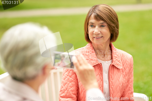 Image of senior woman photographing her friend at park