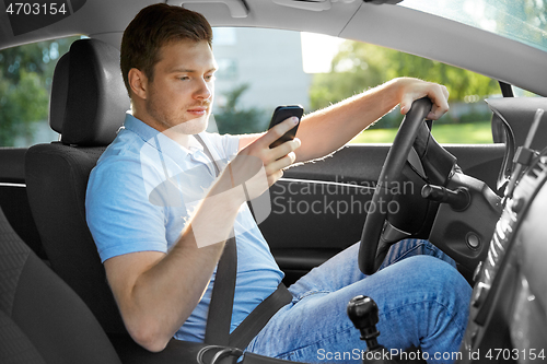 Image of man driving car and using smartphone