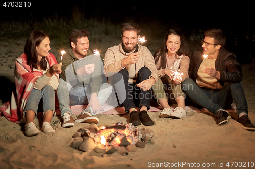 Image of happy friends with sparklers at camp fire at night