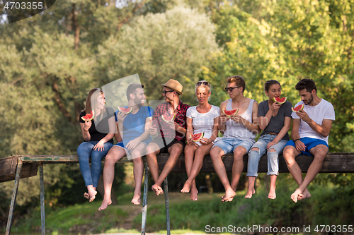 Image of friends enjoying watermelon while sitting on the wooden bridge