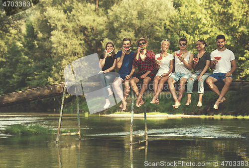 Image of friends enjoying watermelon while sitting on the wooden bridge