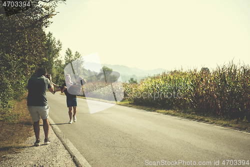 Image of videographer recording while couple jogging along a country road