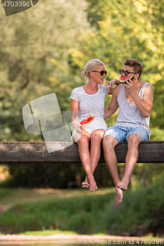 Image of couple enjoying watermelon while sitting on the wooden bridge