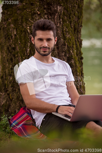 Image of man using a laptop computer on the bank of the river