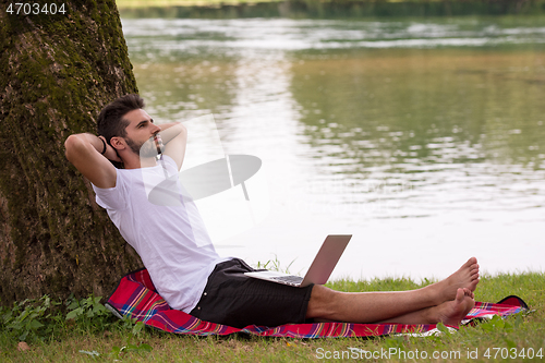 Image of man using a laptop computer on the bank of the river