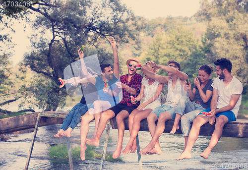 Image of friends enjoying watermelon while sitting on the wooden bridge