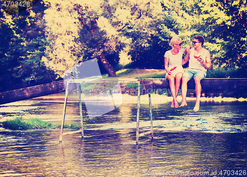 Image of couple enjoying watermelon while sitting on the wooden bridge