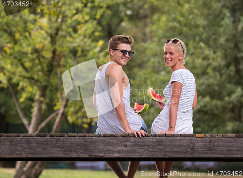 Image of couple enjoying watermelon while sitting on the wooden bridge