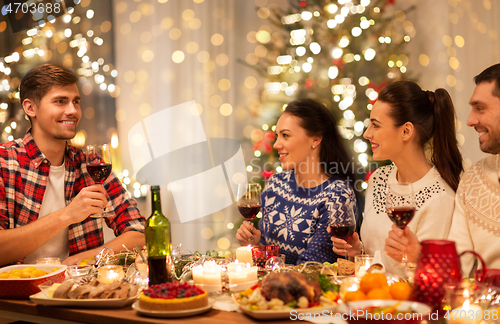 Image of happy friends drinking red wine at christmas party