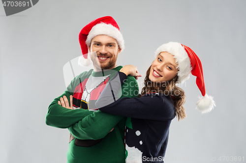 Image of happy couple in christmas sweaters and santa hats