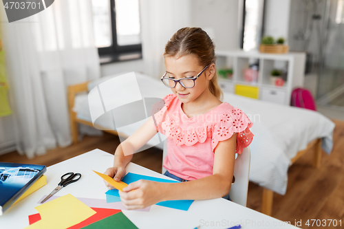 Image of girl with color paper sitting at table at home