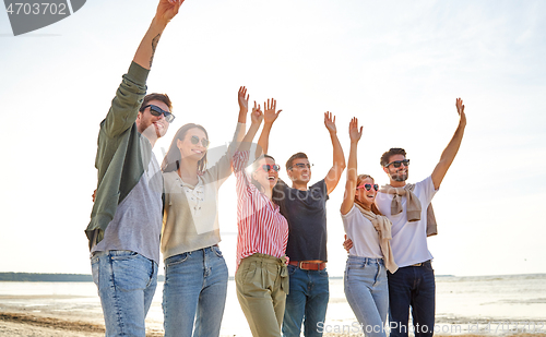 Image of happy friends waving hands on beach in summer