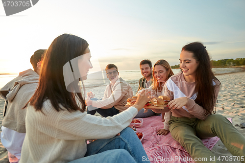 Image of happy friends eating sandwiches at picnic on beach