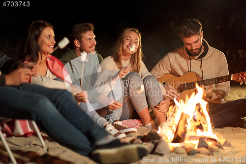 Image of friends roasting marshmallow and playing guitar