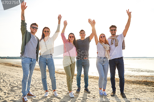 Image of happy friends waving hands on beach in summer