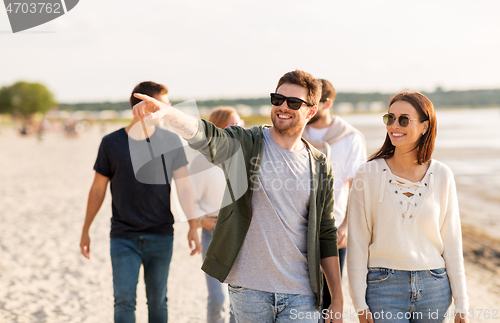 Image of happy friends walking along summer beach