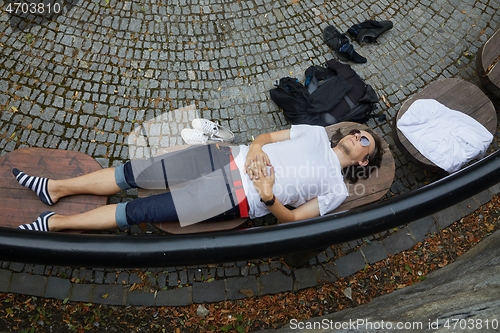 Image of Man lying on a park bench in summer