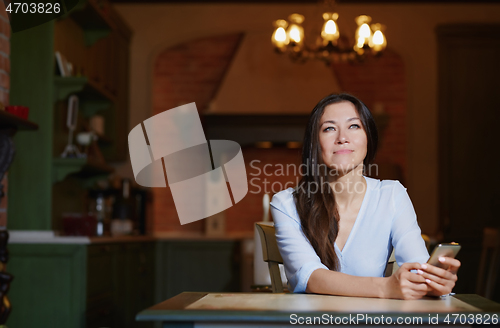 Image of Smiling woman sitting and table and using smartphone