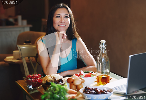 Image of Woman eating healthy food at the table with laptop