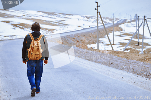 Image of Traveller wearing backpack and walking along rural highway