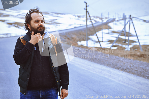 Image of Man with backpack walking along the rural highway