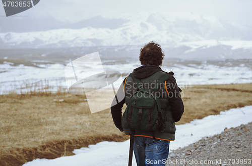 Image of Man wearing backpack and looking at the winter mountains