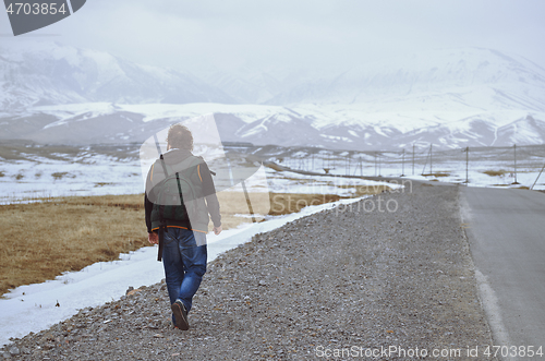 Image of Traveller wearing backpack and walking along rural highway