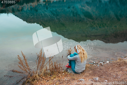 Image of Woman listening music at the water's edge of mountain lake