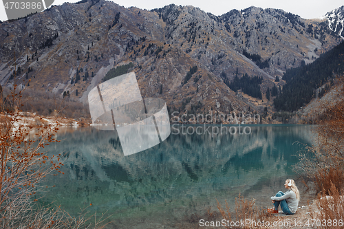 Image of Woman listening music at the water's edge of mountain lake