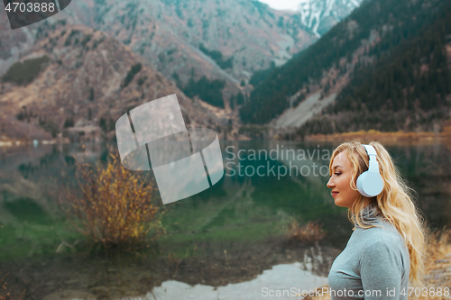 Image of Woman wearing wireless headphones at the mountain lake