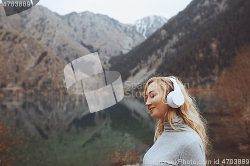 Image of Woman wearing wireless headphones at the mountain lake