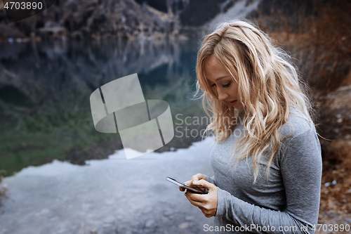 Image of Woman using smartphone at the mountain lake