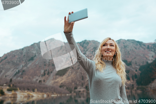 Image of Smiling woman makes selfie at the mountain lake