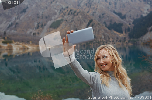 Image of Smiling woman makes selfie at the mountain lake