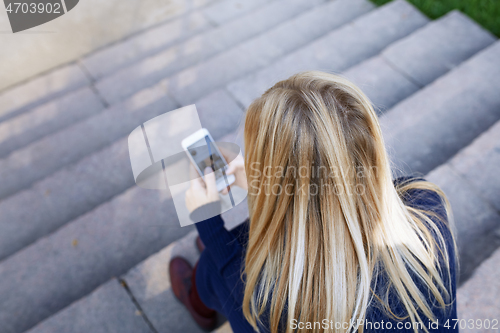 Image of Business woman sitting on city stair steps and holding smartphon