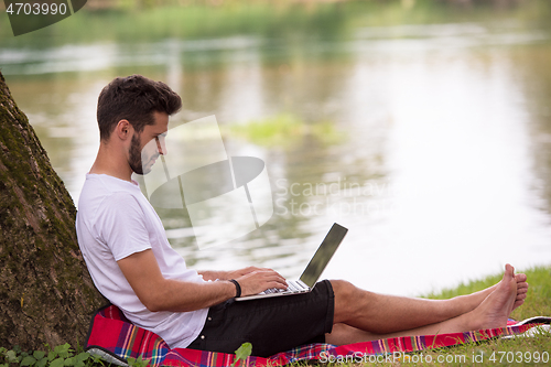 Image of man using a laptop computer on the bank of the river