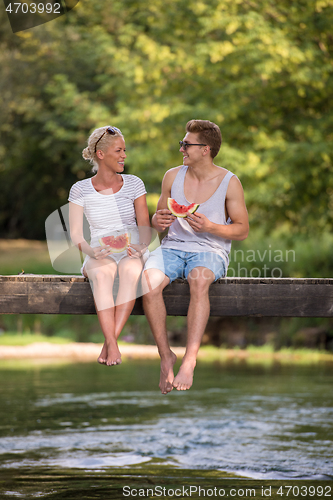 Image of couple enjoying watermelon while sitting on the wooden bridge