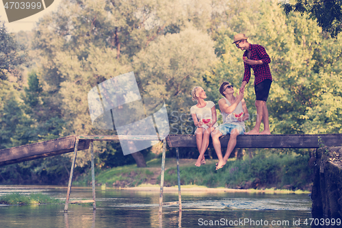 Image of friends enjoying watermelon while sitting on the wooden bridge